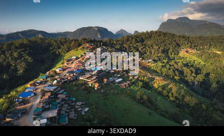 Vista aerea delle tradizionali case in legno del villaggio tribale sulle colline boscose circondate da una lussureggiante foresta tropicale di montagna nel nord della Thailandia durante Foto Stock