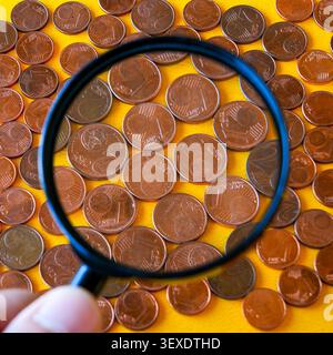 Lente di ingrandimento che esamina le piccole monete in euro e il loro futuro nelle transazioni in contanti quotidiane di oggi Foto Stock
