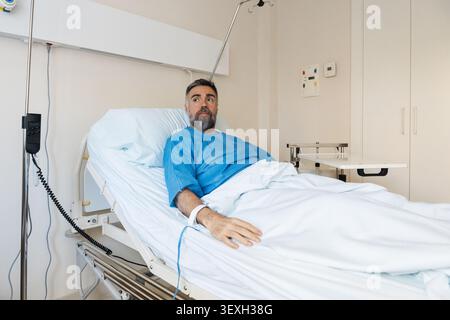 Uomo maturo che si sta riprendendo dalla malattia nel letto d'ospedale Foto Stock
