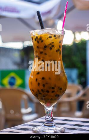 Un vivace e rinfrescante cocktail di caipirinha con frutta della passione brasiliana servito con semi neri freschi, cubetti di ghiaccio e una paglia a scacchi Foto Stock