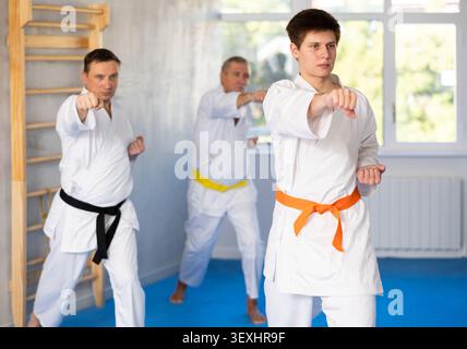 Combatti contro uomini di età diversa durante l'allenamento di karate di gruppo. Guy allena i pugni Foto Stock