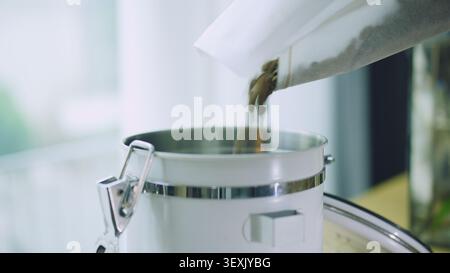Primo piano di travaso di chicchi di caffè torrefatto dal sacchetto al contenitore di conservazione, routine del caffè mattutino Foto Stock