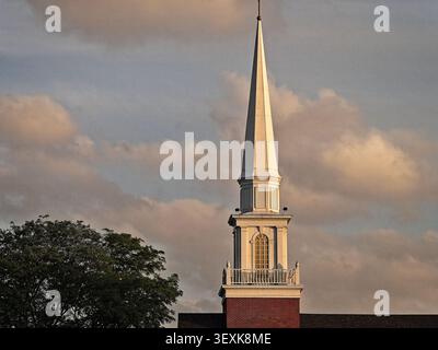 Elegante campanile bianco e torre in mattoni della chiesa che si innalza in un suggestivo cielo nuvoloso illuminato dalla luce dorata del tramonto Foto Stock