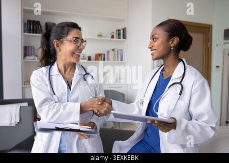 Due medici felici, giovani e anziani, stringono la mano in clinica Foto Stock