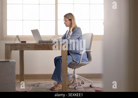Una donna d'affari concentrata si siede alla scrivania a scrivere sul laptop Foto Stock