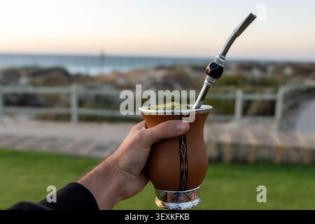 Tenere a mano yerba mate gourd su una spiaggia Foto Stock