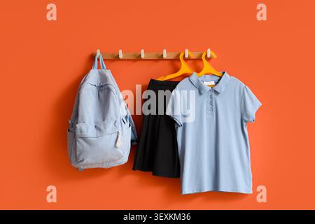 Zaino blu e abiti appesi ai ganci arancioni da parete Foto Stock