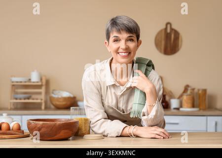 Donna matura sorridente in cucina con asciugamano sulla spalla Foto Stock