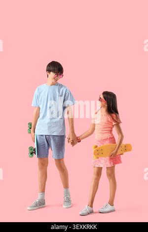 Ragazza carina e suo fratello con skateboard su sfondo rosa Foto Stock