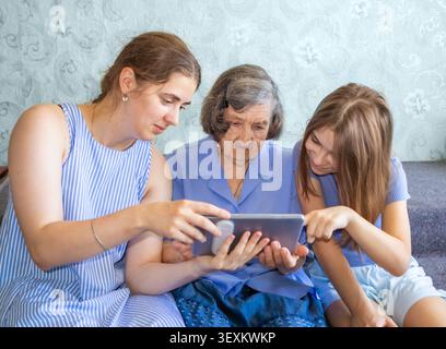 Il legame di famiglia come nipote e figlia insegnano alla nonna di usare un tablet a casa Foto Stock