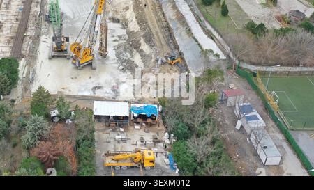 Veduta aerea di un cantiere con macchinari pesanti, gru e camion che operano su un terreno fangoso vicino a un piccolo campo sportivo a Istanbul Foto Stock