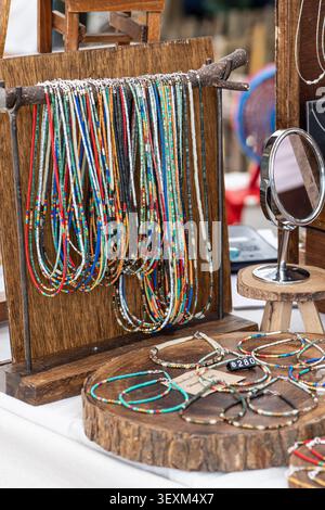 Collane e braccialetti colorati con perle di semi esposti su uno stand di legno presso uno stand di un mercato artigianale Foto Stock