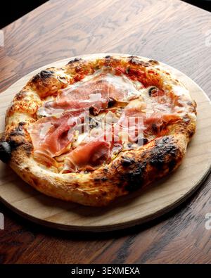 Pizza artigianale con prosciutto, olive e funghi. Isolata su un tavolo di legno. Illuminazione da studio. Foto Stock