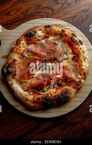 Pizza artigianale con prosciutto, olive e funghi. Isolata su un tavolo di legno. Illuminazione da studio. Foto Stock