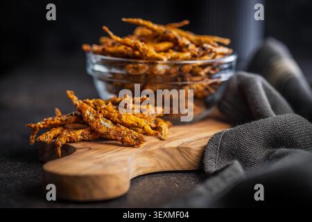 Piccolo pesce fritto dorato servito come spuntino salato su una tavola di legno con una ciotola di vetro in un ambiente rustico e tranquillo. Perfetto per antipasti, tapas Foto Stock