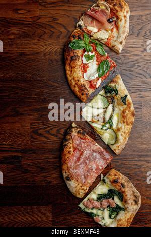 Pizza a fette con vari condimenti disposti in fila. Tavolo di legno. Spazio per il testo. Illuminazione professionale da studio. Foto Stock