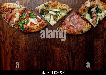 Pizza a fette con vari condimenti disposti in fila. Tavolo di legno. Spazio per il testo. Illuminazione professionale da studio. Foto Stock
