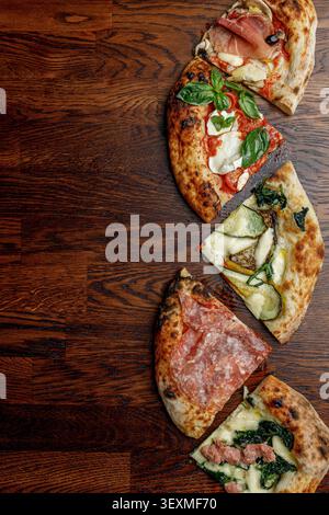 Pizza a fette con vari condimenti disposti in fila. Tavolo di legno. Spazio per il testo. Illuminazione professionale da studio. Foto Stock