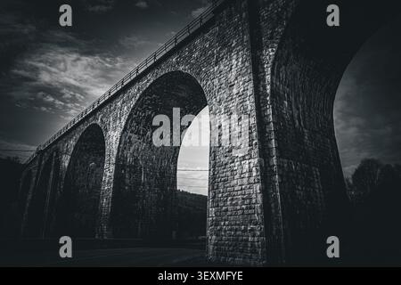 Vista ad angolo basso di un vecchio viadotto ferroviario in pietra in bianco e nero Foto Stock
