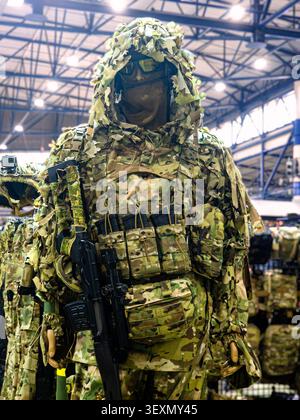 Una divisa da cecchino tattica militare professionale e un set di tute ghillie mostrati su un manichino, con mimetica multicam, sacchetti di munizioni e Foto Stock