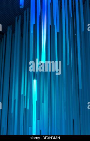 Scatto verticale di un motivo geometrico astratto con pannelli verticali blu illuminati da tubi luminosi al neon. Foto Stock
