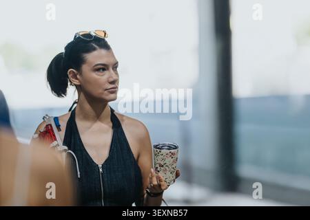 Giovane donna turistica che tiene in mano una tazza da viaggio mentre una troupe di telecamere filma sullo sfondo Foto Stock