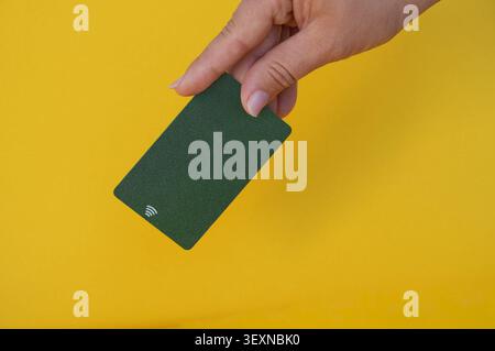 Carta di credito verde in mano su uno sfondo giallo. Spazio per la copia. Foto Stock