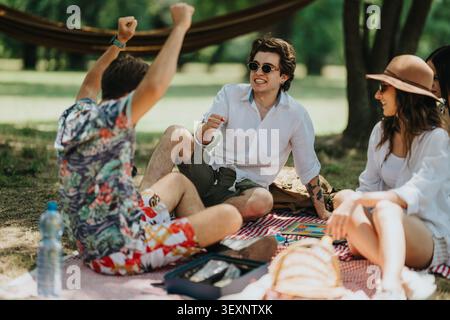 Amici che si godono un rilassante picnic estivo nel parco condividendo giochi e risate su una coperta Foto Stock