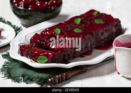Torta fatta in casa con pane al cioccolato condita con salsa di ciliegie, ciliegie fresche e foglie di menta su un piatto da portata. Fotografia di dessert rustici adatta per b Foto Stock