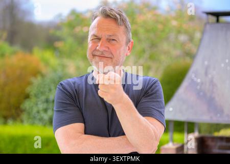 Uomo maturo e sicuro all'aperto che punta verso la fotocamera mentre sorride con un'espressione giocosa. Ritratto naturale di stile di vita con abbigliamento casual, rel Foto Stock