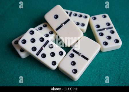 Primo piano di domini bianchi con puntini neri su un tappetino in feltro verde. Piastrelle di gioco disposte in modo ordinato in fila, perfette per il tempo libero, la strategia e i giochi da tavolo Foto Stock