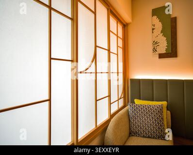 Gli interni delle moderne camere d'hotel giapponesi presentano una finestra curva con schermo shoji, un comodo divano, cuscini a fantasia e un'illuminazione calda e soffusa. Foto Stock
