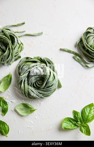 Tagliatelle di spinaci verdi preparate con basilico fresco su una superficie bianca Foto Stock