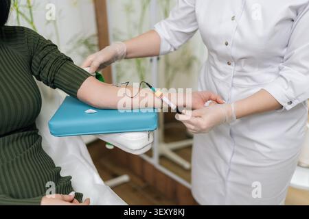 Prima di una flebotomista in clinica che preleva il sangue dal braccio di una donna per un esame di salute, quindi rimuove l'ago farfalla e applica un tampone di cotone Foto Stock