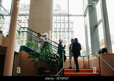 Professionisti che parlano tra di loro mentre si trovano sulle scale dell'edificio degli uffici Foto Stock