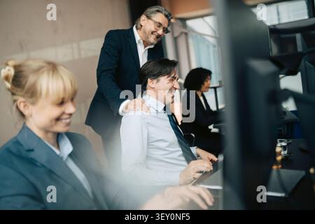 Senior manager che apprezza il dipendente maschile che lavora alla scrivania in ufficio Foto Stock