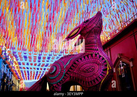 Oaxaca City, Oaxaca, Messico – 7 novembre 2025: Alebrije rosa sotto festoni sospesi Foto Stock