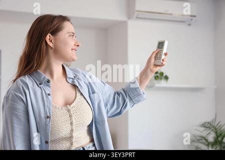 Giovane donna che regola l'aria condizionata con telecomando Foto Stock