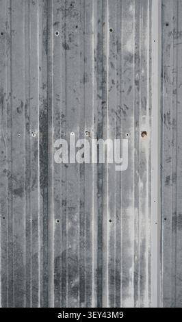 Primo piano verticale del rivestimento in metallo galvanizzato ondulato battuto dalle intemperie con vernice bianca usurata e graffiti neri interrati Foto Stock