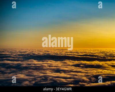 Vista aerea di un denso strato di nuvole bagnato dalla calda luce dorata di un sole che tramonta, con una sfumatura da blu a giallo nel cielo sopra Foto Stock
