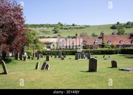 St Mary the Virgin Church a Turville, Buckinghamshire, con lapidi storiche e fiori rosa primaverile contro le Chiltern Hills. Foto Stock