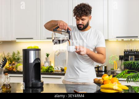 L'uomo arabo versa caffè fresco in una tazza dalla pentola della cucina di casa, brama di caffeina per la routine mattutina. I ragazzi hanno bisogno di un espresso forte e di bevande ogni giorno per rimanere concentrati e vigili sul lavoro. Foto Stock