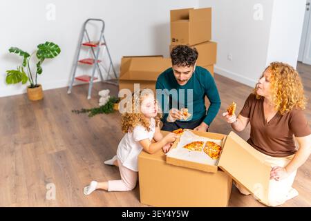 La famiglia si diverte a gustare la pizza in una nuova casa durante il riscaldamento della casa Foto Stock