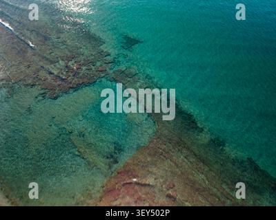 La prospettiva dall'alto verso il basso dei droni cattura le acque turchesi dell'oceano rivelando formazioni rocciose sottomarine e consistenza della barriera corallina. Foto Stock