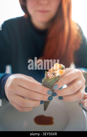Donna che tiene in mano un sushi temaki, gustando la deliziosa cucina giapponese Foto Stock