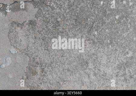 Primo piano ad alta risoluzione di una superficie in calcestruzzo grigio con agenti atmosferici caratterizzata da crepe naturali, texture irregolari e piccoli frammenti di pietra. Ideale per indo Foto Stock