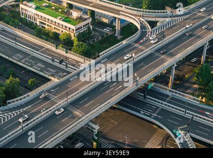 La vista aerea cattura la complessa struttura sopraelevata dell'autostrada che trasporta veicoli in movimento attraverso un moderno paesaggio urbano in Cina al crepuscolo Foto Stock