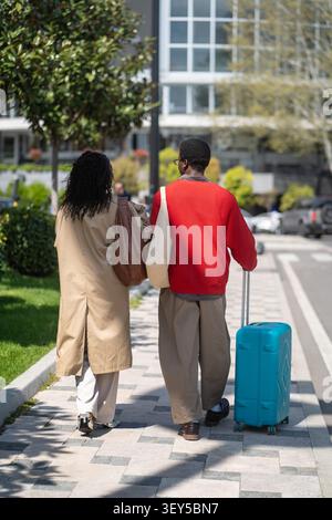Coppia di sposi alla moda, uomini e donne afroamericani che camminano per strada con la valigia. Foto Stock