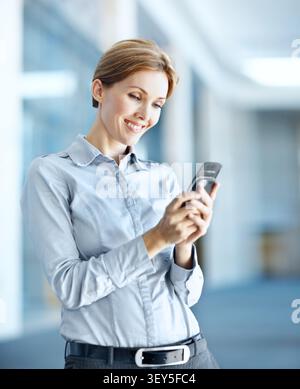 Donna d'affari, sorriso e digitazione in ufficio con telefono, connettività e lettura aggiornamento relazioni pubbliche. Felice, persona e pubblicista sul posto di lavoro con Foto Stock