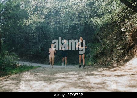 Tre corridori che fanno jogging su un sentiero nella foresta per fitness e allenarsi all'aperto in una giornata di sole Foto Stock